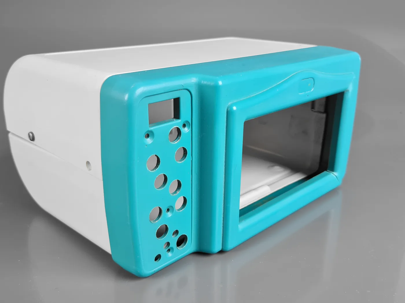 Gabinete termoformado de equipamento em duas cores, corpo branco e moldura frontal turquesa vazada para o comando